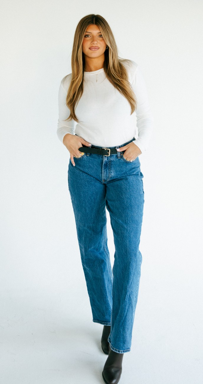 Breck standing in a white sleeveless top and blue jeans in the studio.